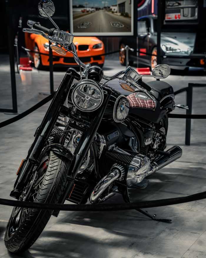A sleek black motorcycle displayed in a vintage car showroom with classic vehicles.